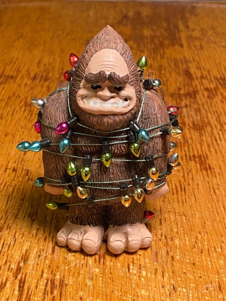 A plastic figuring of Bigfoot covered with a string of Christmas lights.