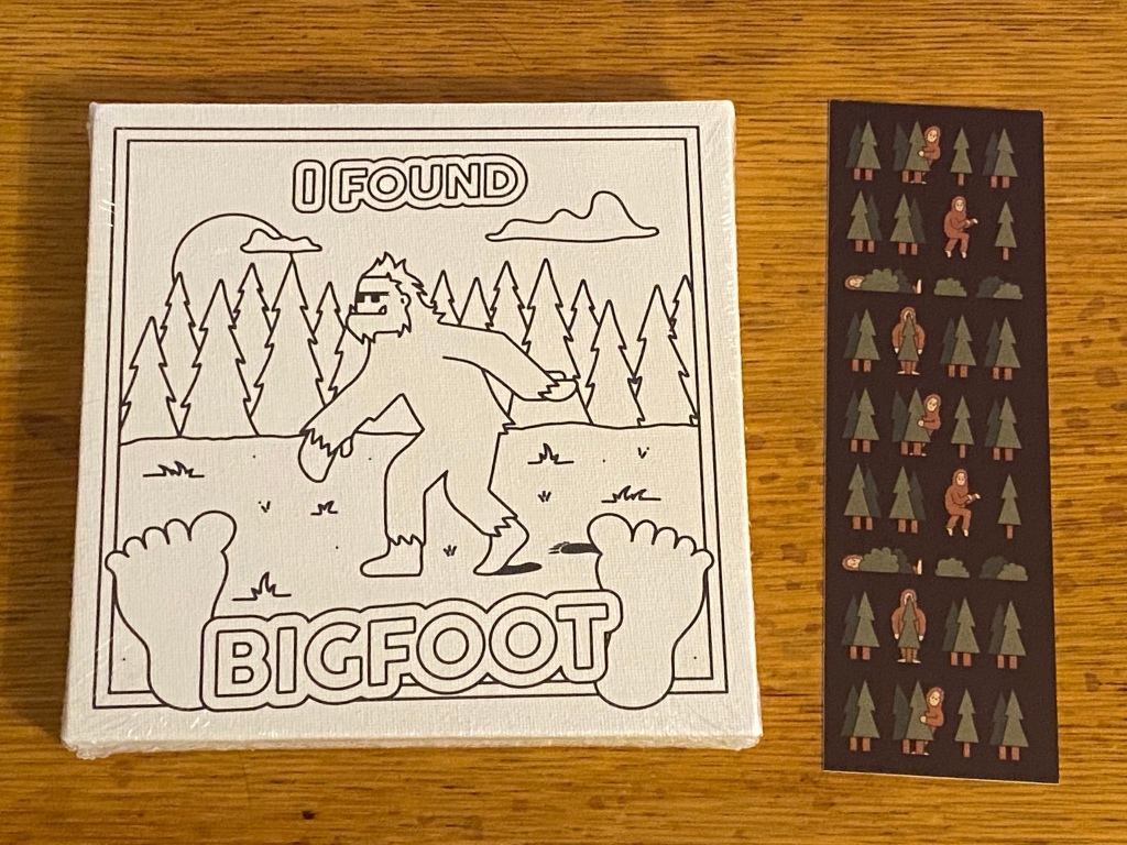 On the left, a small square canvas with an outlined image of Bigfoot and text reading "I found Bigfoot." On the right, a dark brown bookmark decorated with images of trees and Sasquatches.