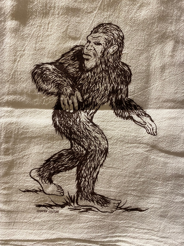 A hand towel with an image of Bigfoot striding to the right and looking over their shoulder.