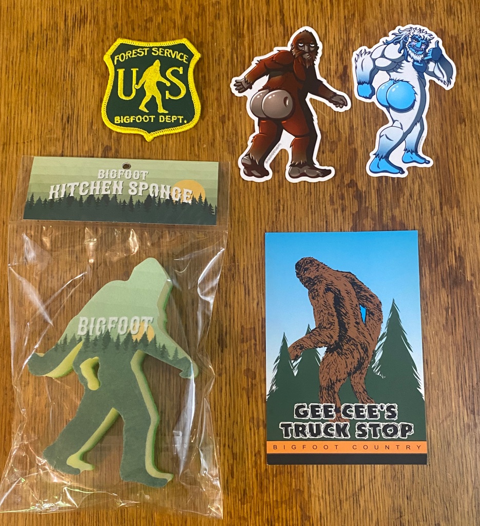 Two sexy Bigfoot stickers, a Bigfoot postcard, a U.S. Forest Service Bigfoot Department patch, and a large kitchen sponge in the shape of a Bigfoot.