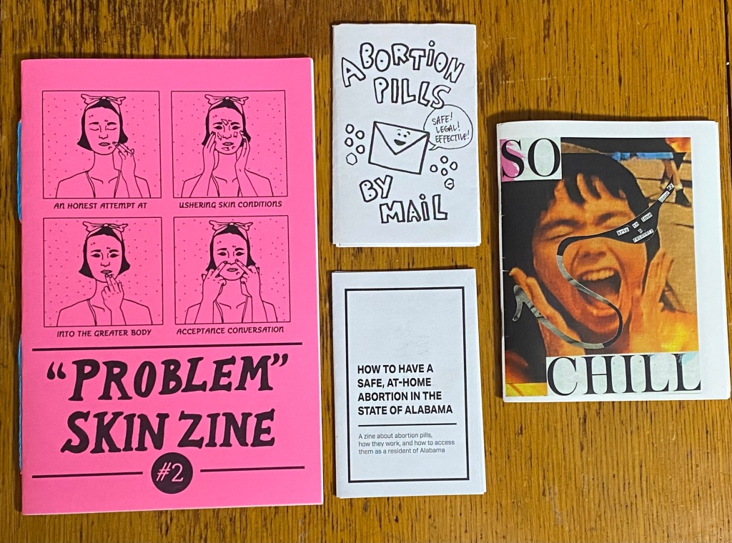 A pink half-size zine with four images of a person doing skin care. Two white minizines. A quarter-size zine with collage images.